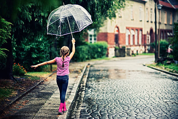 Child holding black umbrella under shower of red hearts