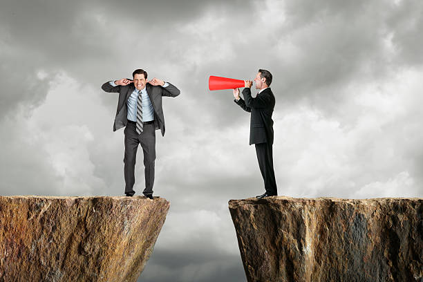 Businessman shouting at another businessman through a megaphone Businessman shouting at business person. hands covering ears stock pictures, royalty-free photos & images