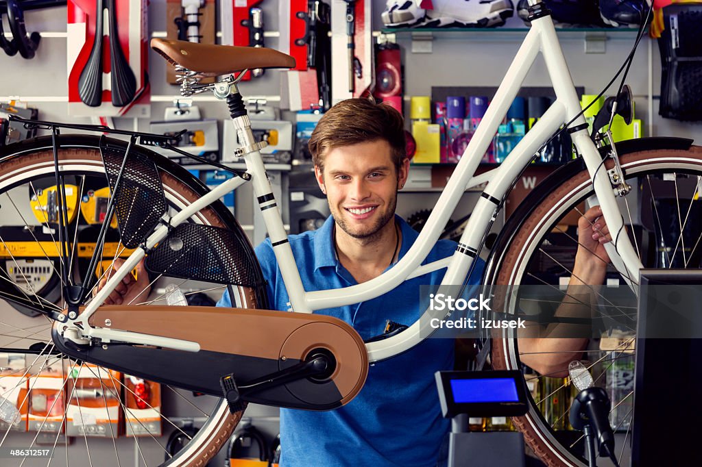 Sales clerk with a bicycle Portrait of young sales clerk in a bike store, holding a bicycle and smiling at camera. 20-24 Years Stock Photo