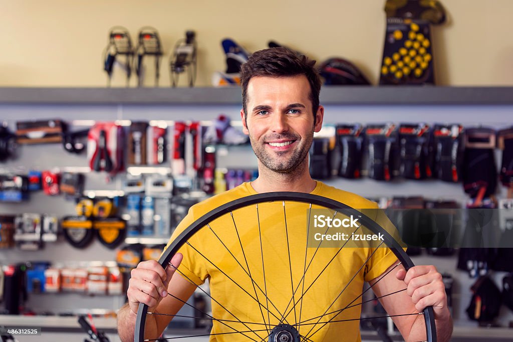 Man with a bicycle wheel Portrait of sales clerk in a sports store, holding a bicycle wheel and smiling at camera. Bicycle Shop Stock Photo