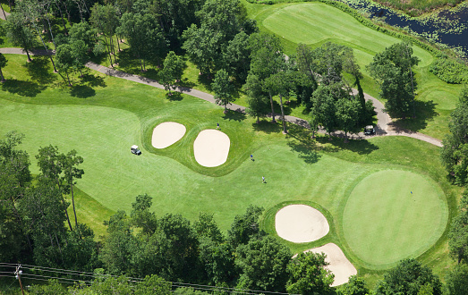 Aerial view of a golf course fairway and green with sand traps, trees and golfers