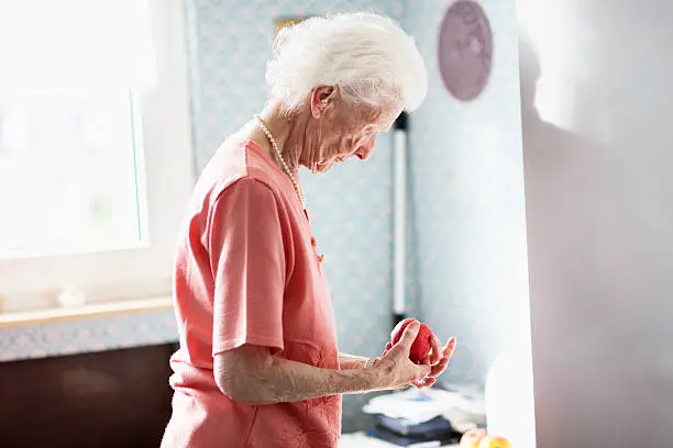 porttrait of a  90 years old woman, in kitchen, with stack of plates, holding an apple