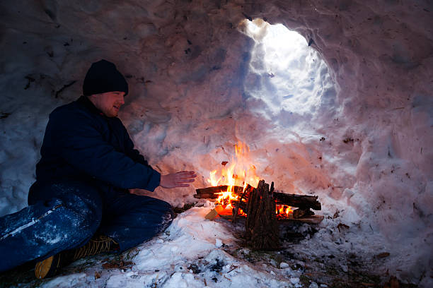 Man warms hands over fire inside igloo Young Caucasian man warms his chilly hands over a flaming fire inside his snow fort igloo during winter camping in Minnesota warms stock pictures, royalty-free photos & images