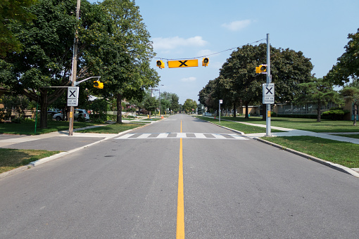 A crosswalk in the middle and on the side in the background, houses on the left and a school on the right.