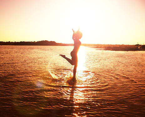 Silhouette of young happy carefree girl jumping on the beach at sunset