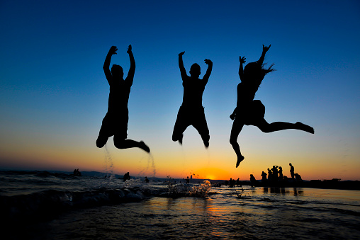 Silhouette of young group of people jumping in ocean at sunset