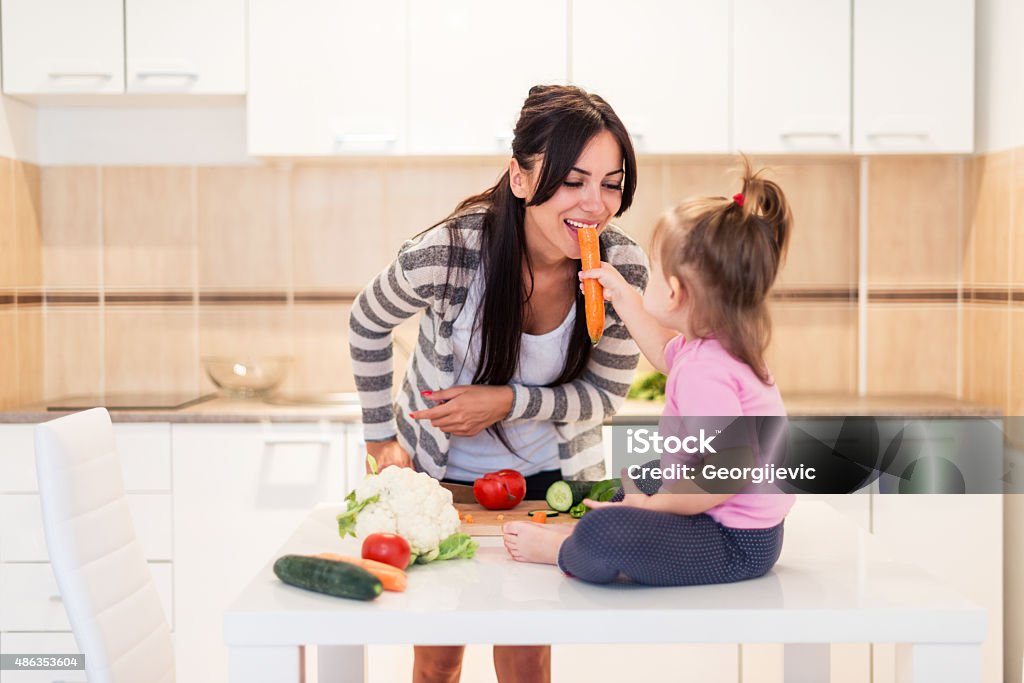 Cheerful toddler Cheerful female toddler feeding her moomy. 2015 Stock Photo