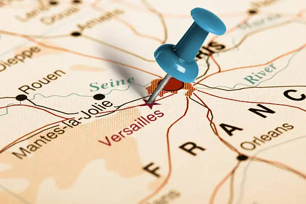 Series: Travel the world, visit landmarks, historical and cultural sights. Blue thumbtack (push pin) that is stuck in a map, which marks Versailles. The map is toned in pastel colors. Concept: Planning travel destinations or journey planning. Close-up view. Studio shot. Landscape orientation.