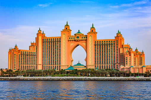 Dubai, United Arab Emirates - April 04, 2012:  Atlantis, The Palm, the luxury five star hotel located on the outer crescent of the man made island, the Palm Jumeirah in the Arabian Gulf city of Dubai, in the United Arab Emirates. In the foreground the waters of the Persian Gulf and date palms transplanted to create a man made garden in front of the hotel. Some traffic and people can also be seen. Photo shot from a boat at an off-shore location, in the afternoon sunlight.  Horizontal format; copy space.