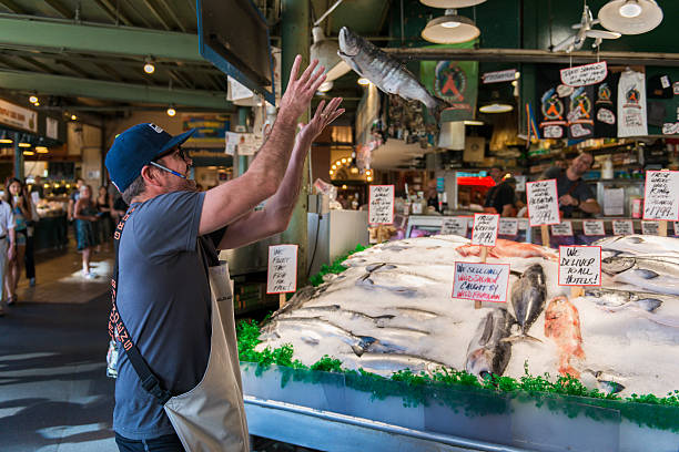 Pike Place Market Seattle, USA - August 18, 2015: A fish Monger at Pike Place Market catching a fish for tourists late in the day. pike place market stock pictures, royalty-free photos & images