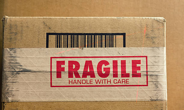 Fragile Handle with Care Fragile sign on shipping box with barcode being read by a thin red laser. fragility stock pictures, royalty-free photos & images