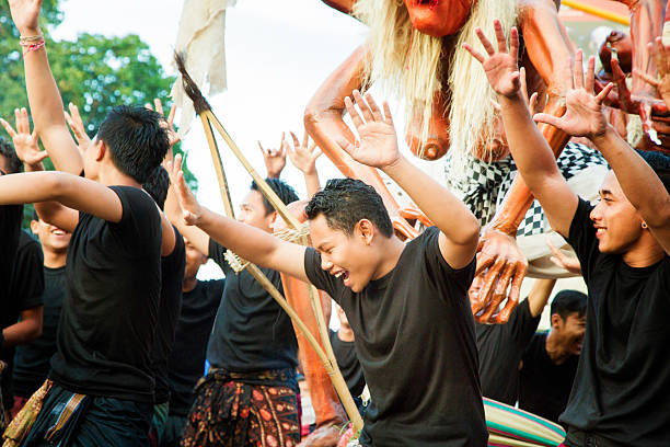 Lovina, Indonesia - March 20, 2015: Young Indonesian men dancing with joy during Nyepi Ngrupuk parade, celebrating the defeat of the ogah-ogah ogre figure, partly seen in the background. Photographed in Lovina, North Bali, Indonesia.