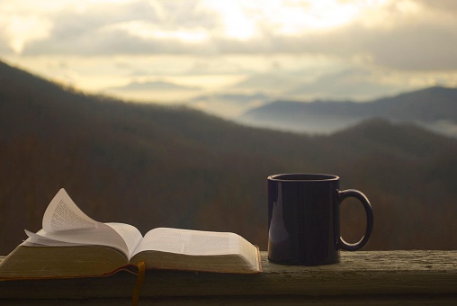 A view of the mountains in the background with a Bible and a coffee mug.