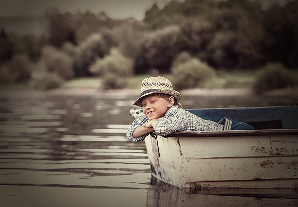Little boy in old boat on the calm lake surface 
