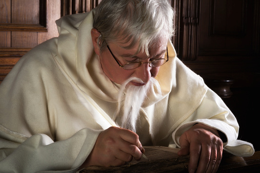 Monk with gray beard writing in an ancient book