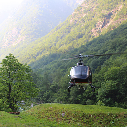 Helicopter hovers above grassy landing area, in mountains