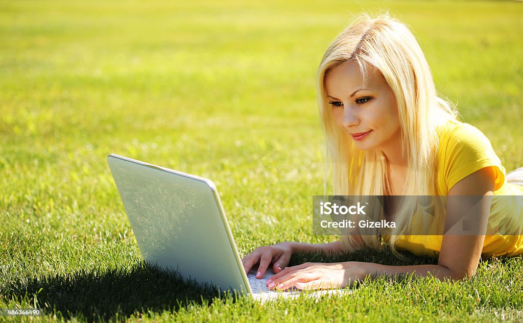 Blonde Girl with Laptop. Smiling Beautiful Woman Blonde Girl with Laptop. Smiling Beautiful Woman Lying on Green Grass. Outdoor 2015 Stock Photo