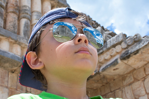 Low angle closeup of young tourist wearing high reflective sunglasses showing majestic Maya pyramid at archaeological site of Uxmal, Yucatan, Mexico