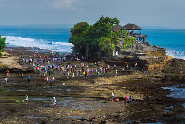 Bali, Indonesia - April 19, 2015: Tourists walking around Tanah Lot temple during low tide at Bali Indonesia, April 19,2015