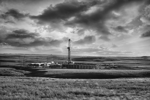 Fracking Drill Rig in a remote location on the prairie in a hay field with bales. with wispy clouds in the sky at dusk.  Fracking Rig is performing a fracking operation to liberate trapped crude oil and natural gas into the pipeline to a refinery.
