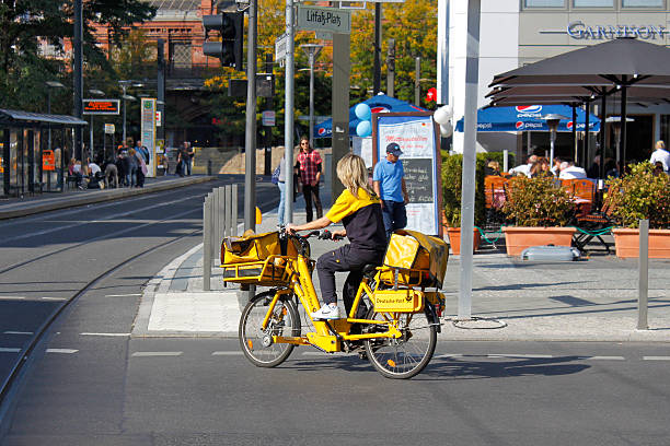 Berlin, Germany - September 24, 2011: Postwoman moves on her yellow bike on a city street and deliver mail.