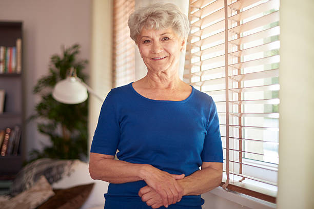 Cheerful grandmother standing next to the window Cheerful grandmother standing next to the window grandma portrait stock pictures, royalty-free photos & images