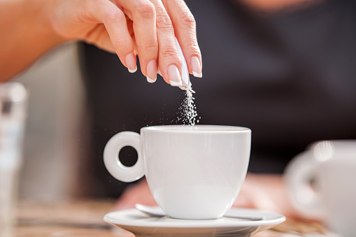 Woman's hand pouring sugar in her coffee.