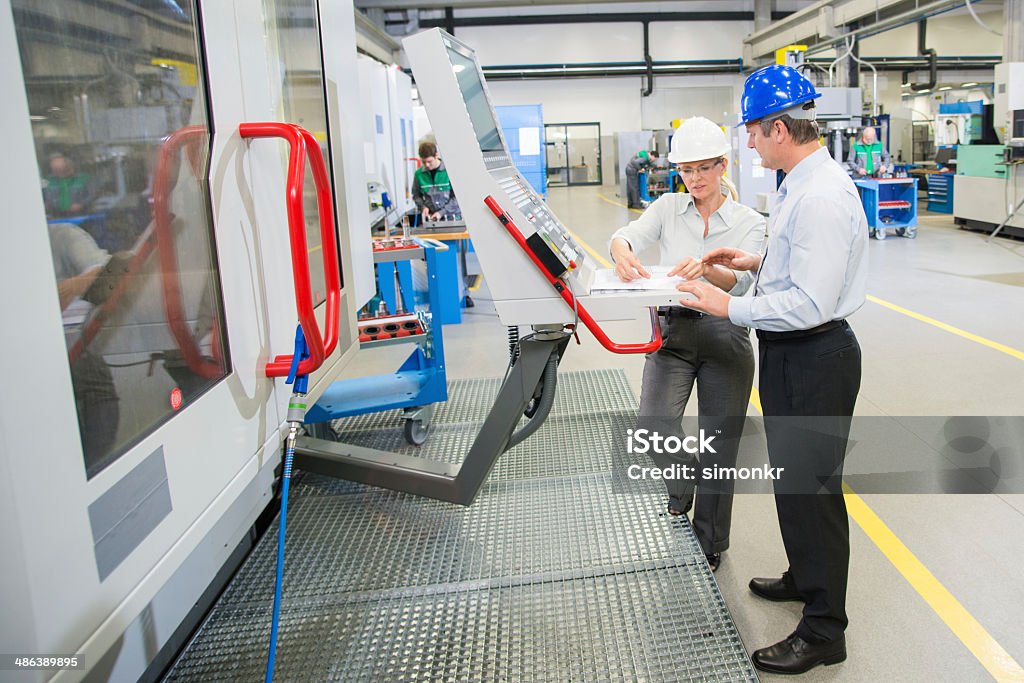 Manager And Engineer Programming A CNC Mid-adult male manager and a female engineer programming a CNC machine at the manufacturing plant. Machinery Stock Photo