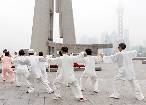 Shanghai, China - May 14, 2012: Men and women participate in unison in early morning Tai Chi near the Bund with the skyscrapers of Pudong beyond in the smog