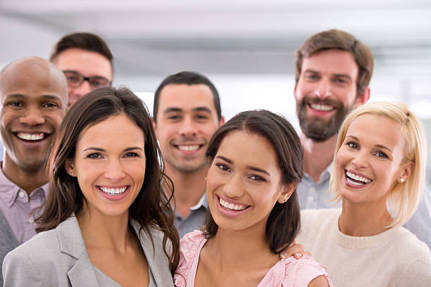 Closeup portrait of goofy mid 20's people having fun.Standing in a row with their arms raised,laughing and looking at camera.All wearing casual clothes.The closest girl is in focus.She's wearing coral colored shirt.