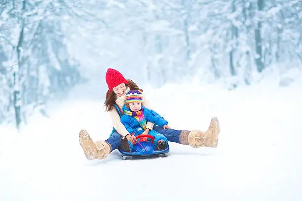 Young mother and her little toddler daughter enjoying a sledge ride in a snowy park