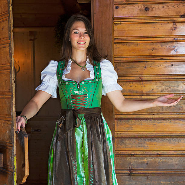 dirndl mujer de pie en puerta con gesto de bienvenida - alm bavaria mountain summer fotografías e imágenes de stock