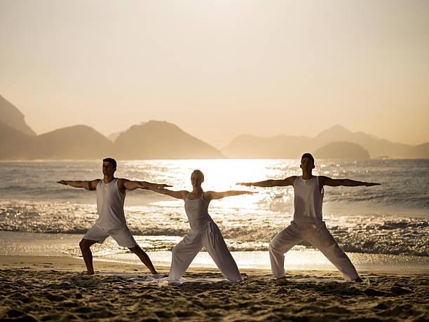 istock People doing Yoga exercises on the beach at sunset. 486400858