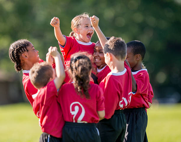 Little Girl Cheering in Team Huddle A multi-ethnic soccer team full of elementary age children are cheering together after winning their game. They have their arms raised up in the air victoriously. team sport stock pictures, royalty-free photos & images