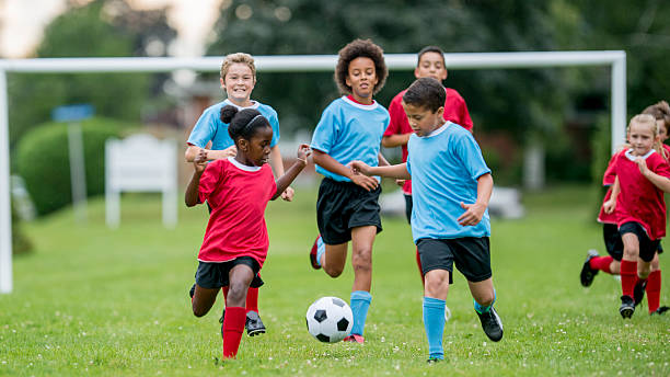 Children Chasing Soccer Ball During a Match A multi-ethnic group of children are playing soccer, while running down a grass field, kicking and chasing the ball. sports activity stock pictures, royalty-free photos & images