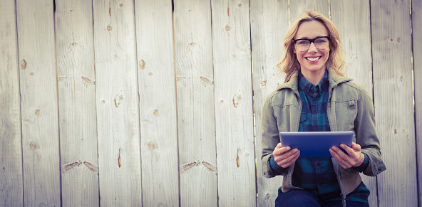 Smiling blonde in glasses using tablet pc against bleached wooden planks