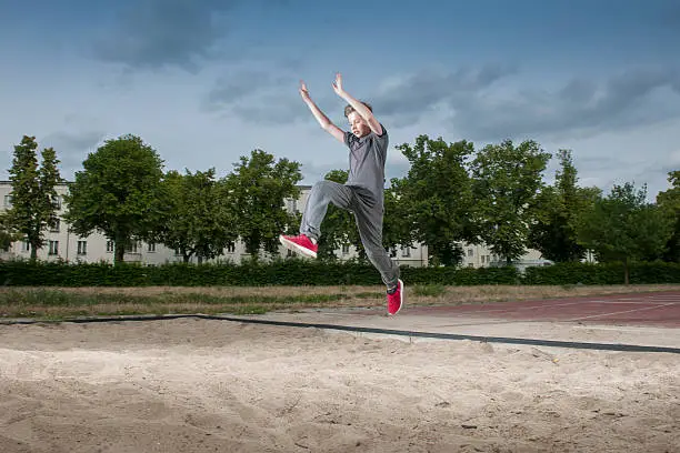 frozen side frontal full body view of a male young teenagers jumping into a long jump pit