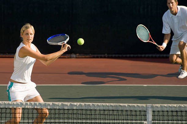 istock Tennis Player Hitting Ball With Partner Standing In Background 486415089