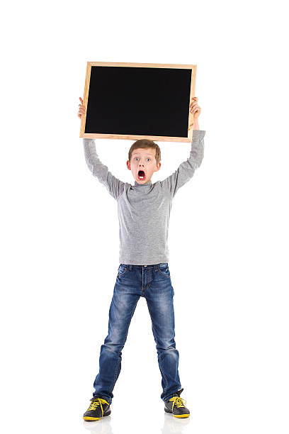 Shouting schoolboy with balckboard Shocked schoolboy holding blackboard over his head. Full length studio shot isolated on white. blackboard child shock screaming stock pictures, royalty-free photos & images
