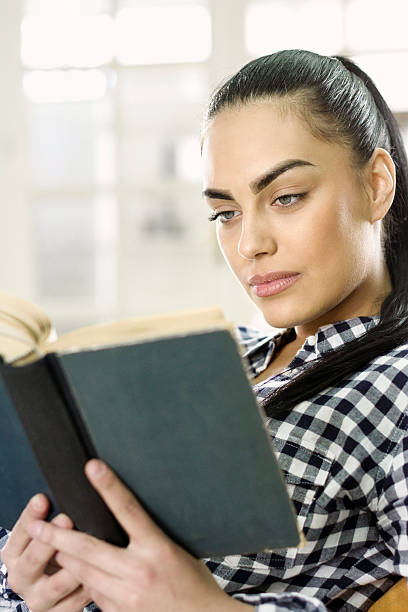 istock Young woman on sofa reading a book 486427144