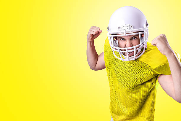 football-spieler im gelben trikot auf gelbem hintergrund - football helmet american football yellow american football uniform stock-fotos und bilder