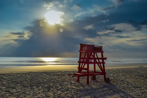 An empty red lifeguard beach at dawn with a spectacular sunrise in the clouds reflected in the waves .