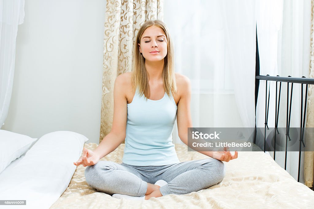 Woman meditating Beautiful blonde woman is meditating on bed in her bedroom. 20-24 Years Stock Photo