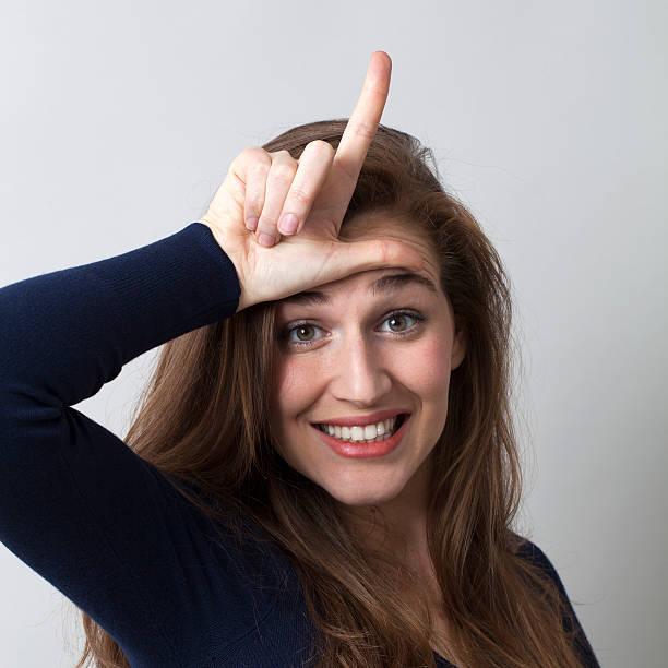 istock smiling 20s girl with L on forehead for loser sign 486446834