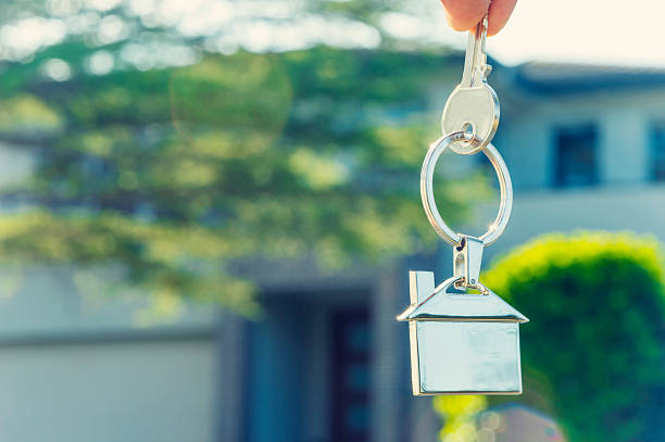 istock Hand holding house key in front of a large house. 486449190