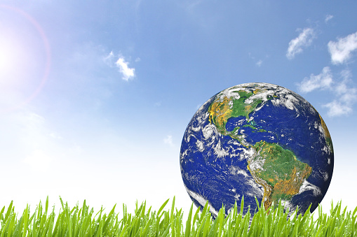 Planet Earth on beautiful green grass and sunny day with blue cloudy sky - Elements of this image furnished by NASA