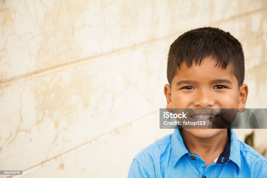 Headshot of cute Latin or Asian boy. Copyspace. Headshot of cute little Latin or Asian descent boy outdoors in front of a tan colored, textured wall. The elementary age boy wears a big smile and a blue collared shirt. Copyspace to left.  Portrait, close-up style image. Child Stock Photo