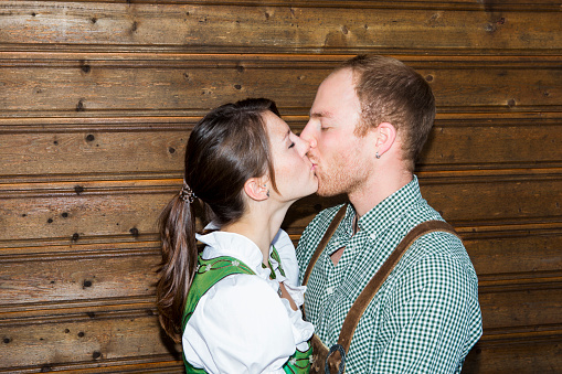 bavarian couple kissing each other in front of wooden wall