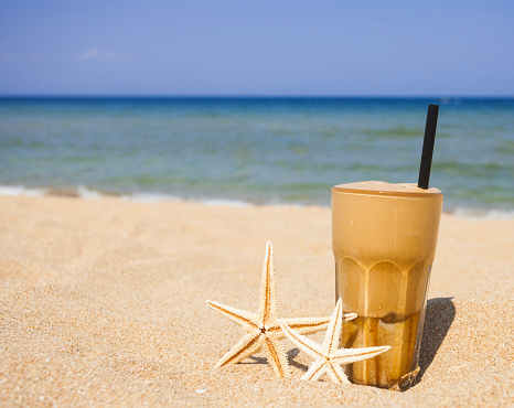 Iced coffee and starfishes on a sandy beach background