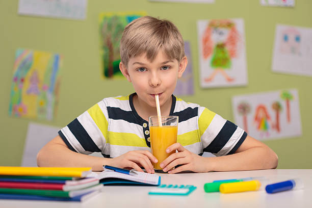 Schoolboy sitting at school desk Schoolboy sitting at school desk and drinking orange juice food elementary student healthy eating schoolboy stock pictures, royalty-free photos & images